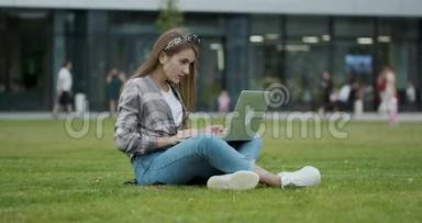 年轻的女学生在露天坐时使用笔记本电脑。 女孩用笔记本电脑查找资料